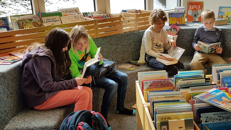 Kinder sitzen lesend auf der runden Bibliotheksbank.