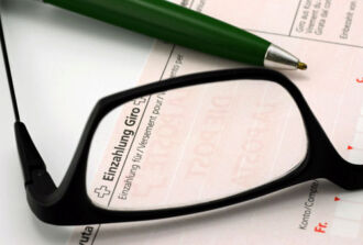 Bild von einem Teil eines Einzahlungsscheines, auf dem ein Kugelschreiber und eine Brille liegt