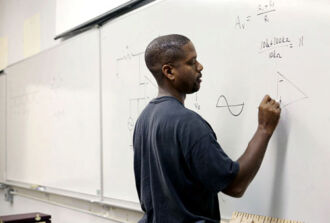 Schwarzer Mittelstufenschüler steht am Witebord und schreibt eine Formel auf.