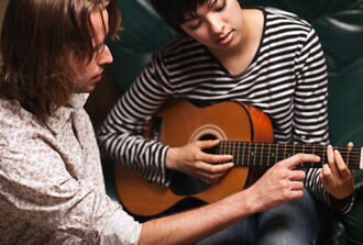 Gitarrenlehrer unterrichtet eine Schülerin.
