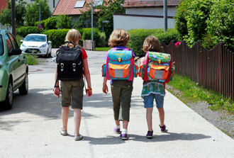 Drei Schulkinder gehen gemeinsam mit ihren Schultheken auf einer Quartierstrasse.