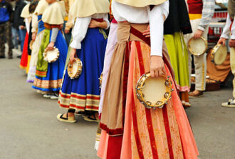 Frauen stehen in fremdländischen Trachten mit einer Tabourinrassel zum Traditionsfest bereit.