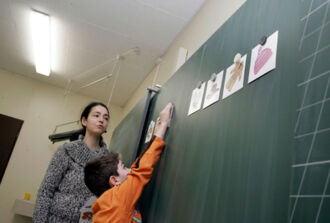 Schulkind zeigt auf ein an der Tafel aufgehängtes Bild eines Alltaggegenstands um das Wort dafür zu lernen.