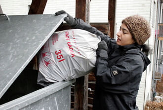 Eine Frau entsorgt einen Gebührensack im Abfallcontainer.