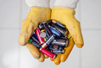 Zwei behandschuhte Hände halten viele leere Batterien.